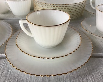 May include: A set of white milk glass teacups and saucers with a gold trim. The cups and saucers have a fluted design.