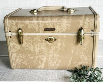 May include: A vintage tan Samsonite hard-sided suitcase with gold-toned hardware and a lock. The suitcase has a textured surface and a white trim around the edges.