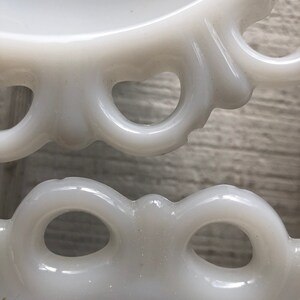 May include: White milk glass pedestal with a scalloped edge and openwork design. The pedestal has a smooth, glossy finish.