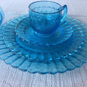 May include: A set of blue glass dishes with a scalloped edge and a textured surface. The set includes a teacup, saucer, and two plates.
