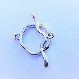 May include: Silver-toned metal clasp with a circular design and a curved bar. The clasp is designed to be used for necklaces or bracelets.