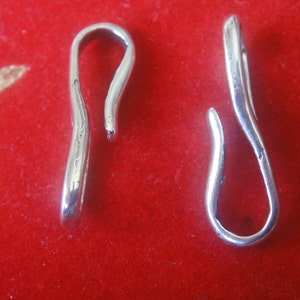 May include: Two silver-toned metal clasps with a loop on one end and a hook on the other end. The clasps are on a red background.