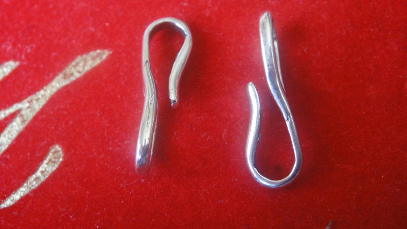 May include: Two silver-toned metal clasps with a loop on one end and a hook on the other end. The clasps are on a red background.