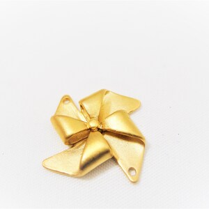 May include: A gold-colored metal bow charm with two holes for attaching to jewelry or other crafts.