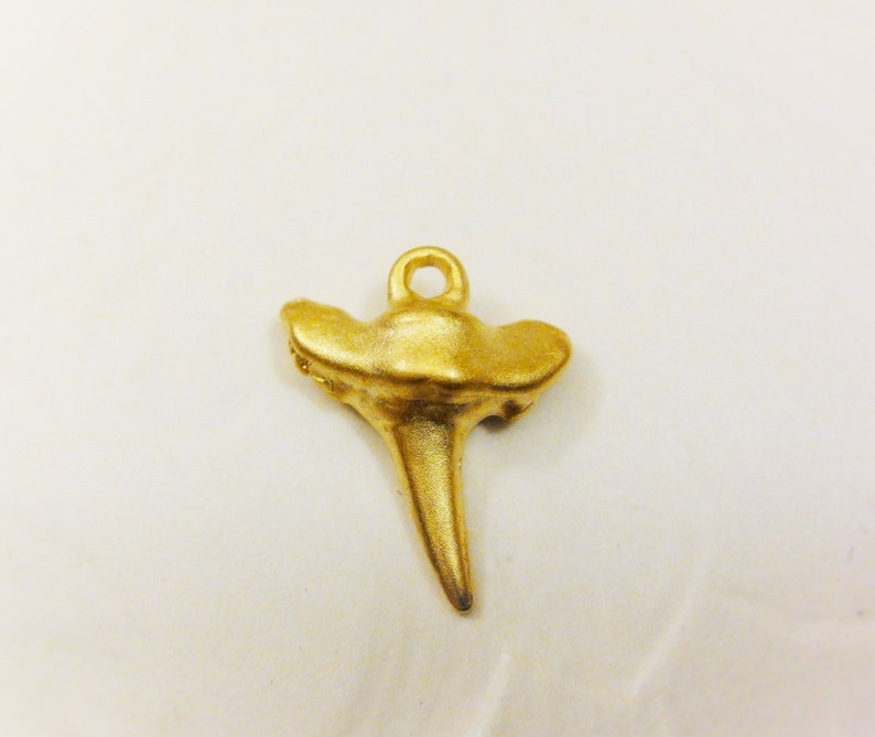 May include: Gold-colored metal shark tooth pendant charm with a loop at the top for attaching to a necklace or bracelet.