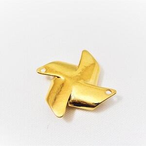 May include: Gold-colored metal charm shaped like a four-pointed star with rounded edges. The charm has two small holes on each point.
