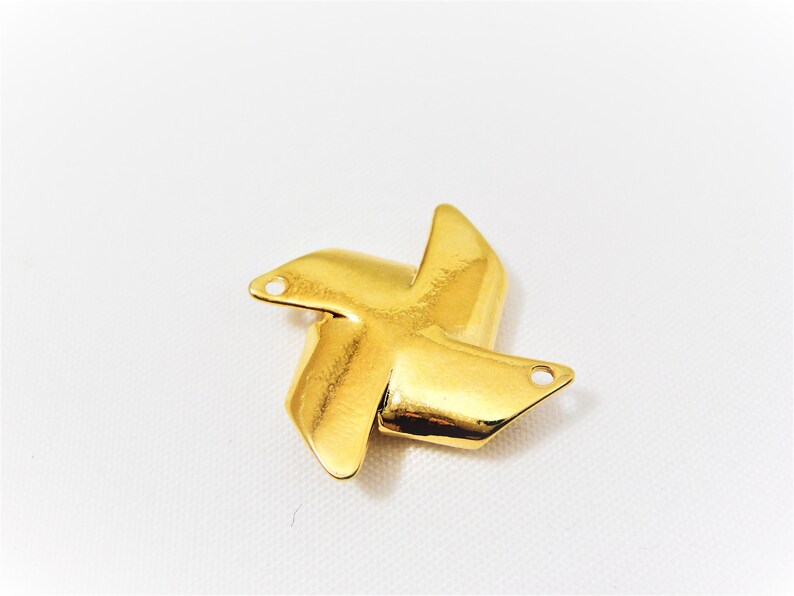 May include: Gold-colored metal charm shaped like a four-pointed star with rounded edges. The charm has two small holes on each point.