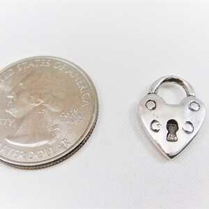 以下が含まれることがあります： アメリカの25セント硬貨と並べてサイズ比較した、銀製のハート型の南京錠チャームです。