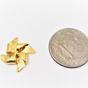 May include: Gold-colored metal pinwheel charm with a decorative bow design. The charm is about the size of a US quarter.