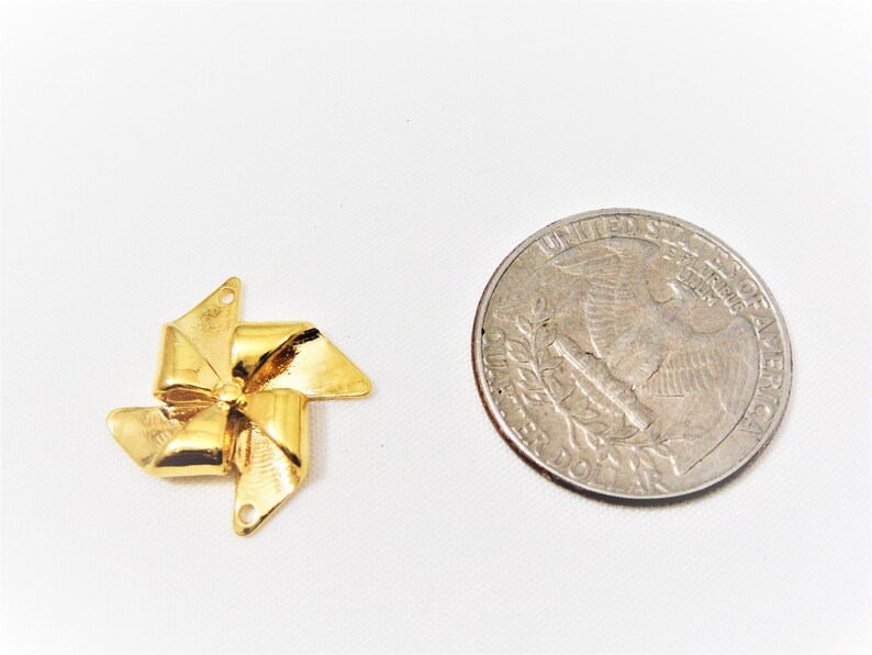 May include: Gold-colored metal pinwheel charm with a decorative bow design. The charm is about the size of a US quarter.