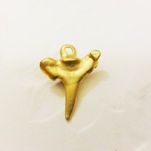 May include: A gold-colored pendant shaped like a shark tooth. The pendant has a loop at the top for attaching to a chain.