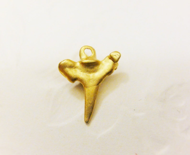 May include: A gold-colored pendant shaped like a shark tooth. The pendant has a loop at the top for attaching to a chain.