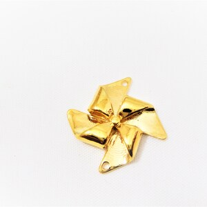 May include: A gold-colored metal pinwheel charm with a five-pointed star shape. The pinwheel has a hole at the top for attaching to a necklace or bracelet.