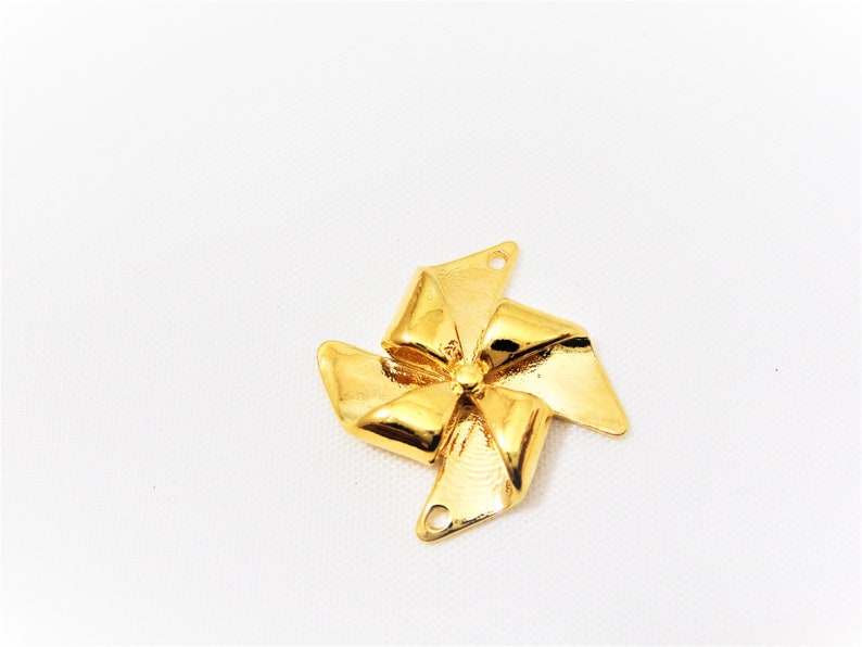 May include: A gold-colored metal pinwheel charm with a five-pointed star shape. The pinwheel has a hole at the top for attaching to a necklace or bracelet.