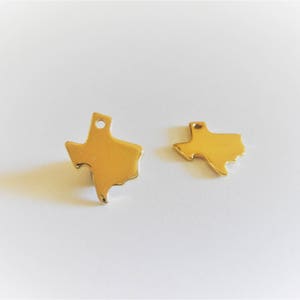 May include: Two gold-colored metal charms shaped like the state of Texas. The charms are different sizes.