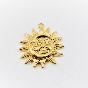 May include: Gold-toned pendant charm featuring a sun with a face and a crescent moon. The sun has a stylized face with a smile and eyes.