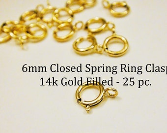 May include: A close-up of 25 gold-filled 6mm closed spring ring clasps. 6mm Closed Spring Ring Clasps 14k Gold Filled - 25 pc.
