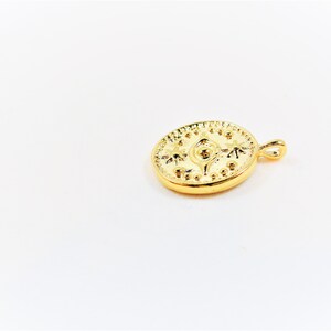May include: Gold-toned pendant featuring a circular design with an eye and star-like shapes. The pendant has a small loop at the top for attaching to a chain.