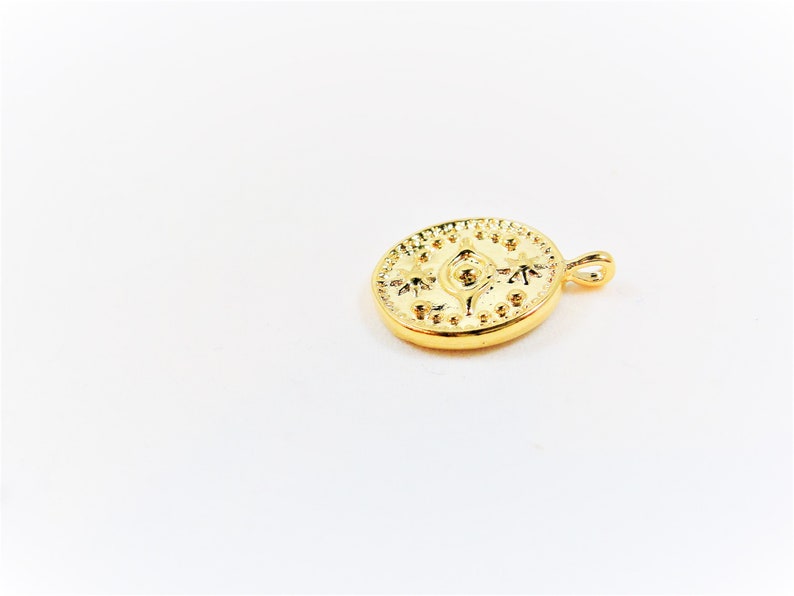 May include: Gold-toned pendant featuring a circular design with an eye and star-like shapes. The pendant has a small loop at the top for attaching to a chain.