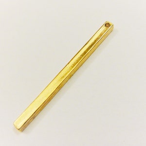 May include: A gold-colored metal bar with a hole at the top. The bar is about 2 inches long and has a rectangular shape.