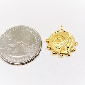 May include: Gold-toned pendant featuring a cherub with wings, surrounded by small beads. The pendant is about the size of a UK 20 pence coin.