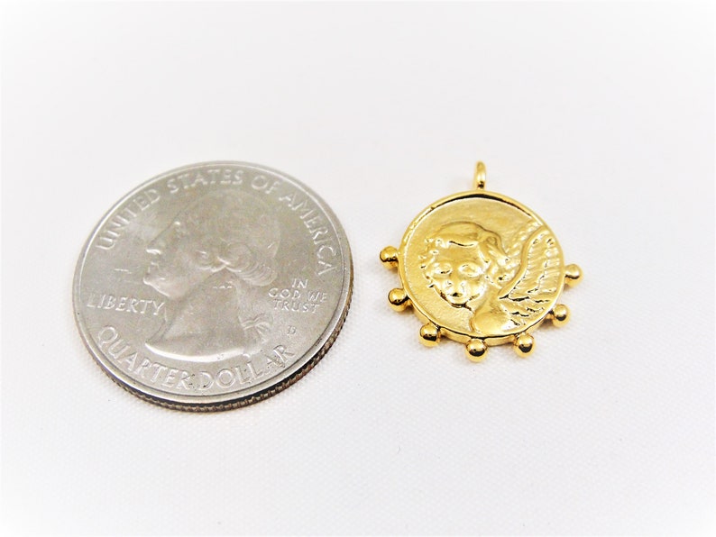 May include: Gold-toned pendant featuring a cherub with wings, surrounded by small beads. The pendant is about the size of a UK 20 pence coin.