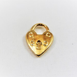 以下が含まれることがあります： 鍵穴のある金色のハート型の南京錠チャーム。南京錠は両側に2つの装飾的な円があります。