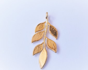 May include: A gold-colored leaf pendant with a textured surface. The pendant features a stem with several detailed leaves. The jewelry piece is designed to be worn as a necklace charm or earring component.