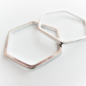 May include: Two silver hexagonal rings, one slightly larger than the other, are stacked on top of each other. The rings are smooth and have a polished finish.