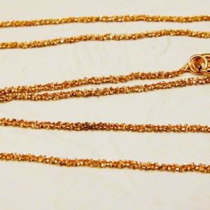Puede incluir: Un collar de cadena de oro con un dise&ntilde;o delicado y trenzado. La cadena est&aacute; hecha de peque&ntilde;os eslabones redondos que est&aacute;n estrechamente entrelazados.