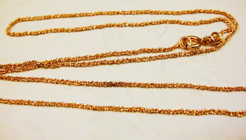 Puede incluir: Un collar de cadena de oro con un dise&ntilde;o delicado y trenzado. La cadena est&aacute; hecha de peque&ntilde;os eslabones redondos que est&aacute;n estrechamente entrelazados.