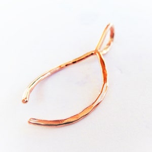 May include: A rose gold wishbone pendant charm. The charm is made of wire and has a hammered texture.
