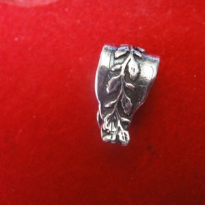 May include: Silver charm with a detailed design of a leafy branch. The charm is a pendant or a bead for a necklace or bracelet.