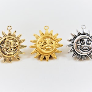 May include: Three sun and moon charms with a face design. The charms are gold, silver, and a darker silver color. The charms are all the same design, but in different colors.