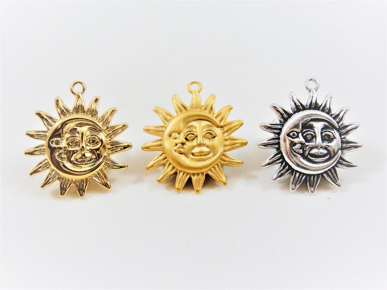 May include: Three sun and moon charms with a face design. The charms are gold, silver, and a darker silver color. The charms are all the same design, but in different colors.