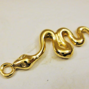 May include: A gold-colored snake charm with a loop for attaching to a necklace or bracelet. The snake is curled in a realistic pose.