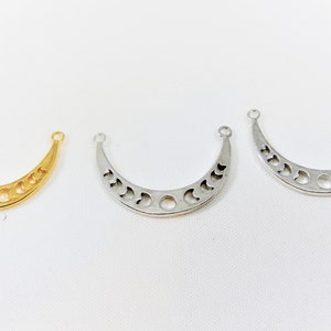 May include: Three crescent moon shaped metal charms with cut-out moon phases. The charms are gold, silver, and a lighter silver color.