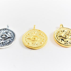 May include: Three round pendants with an eye design and star accents. The pendants are silver, gold, and gold.