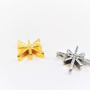 May include: Two star-shaped metal charms, one gold and one silver. Both charms have a textured surface.