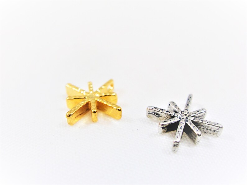 May include: Two star-shaped metal charms, one gold and one silver. Both charms have a textured surface.