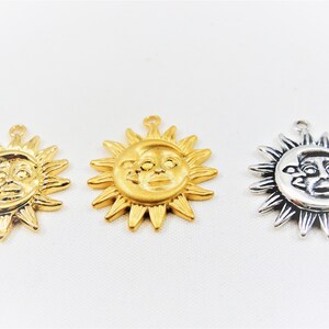 May include: Three gold-toned sun charms with a face in the center. The sun charms have a loop at the top for hanging.