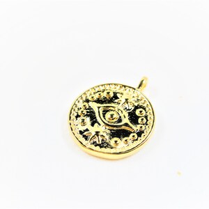 May include: Gold-toned pendant featuring a detailed eye design with a circular shape and a small loop at the top for attaching to a chain.