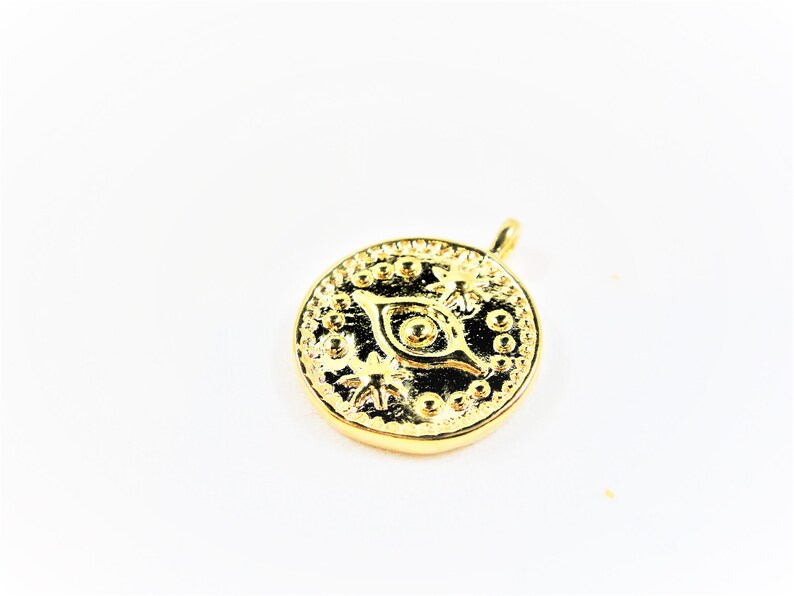 May include: Gold-toned pendant featuring a detailed eye design with a circular shape and a small loop at the top for attaching to a chain.
