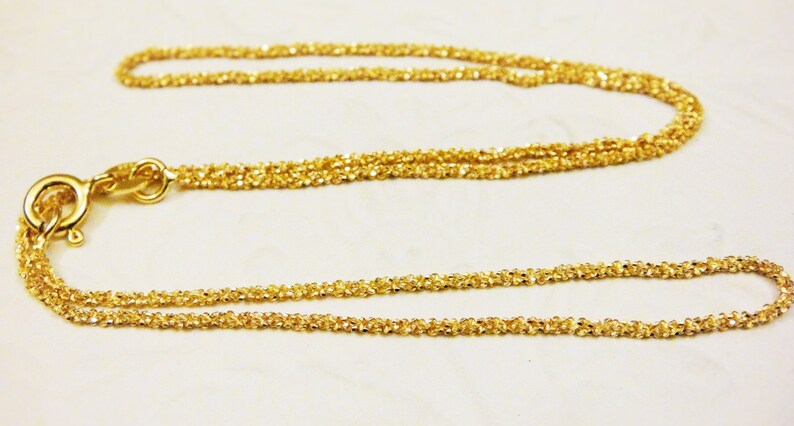 May include: A gold chain necklace with a delicate, twisted design. The chain is made of multiple strands of thin, interwoven wire.