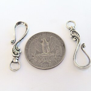 May include: Two silver-toned metal clasps with ornate designs. The clasps are about the size of a US quarter.