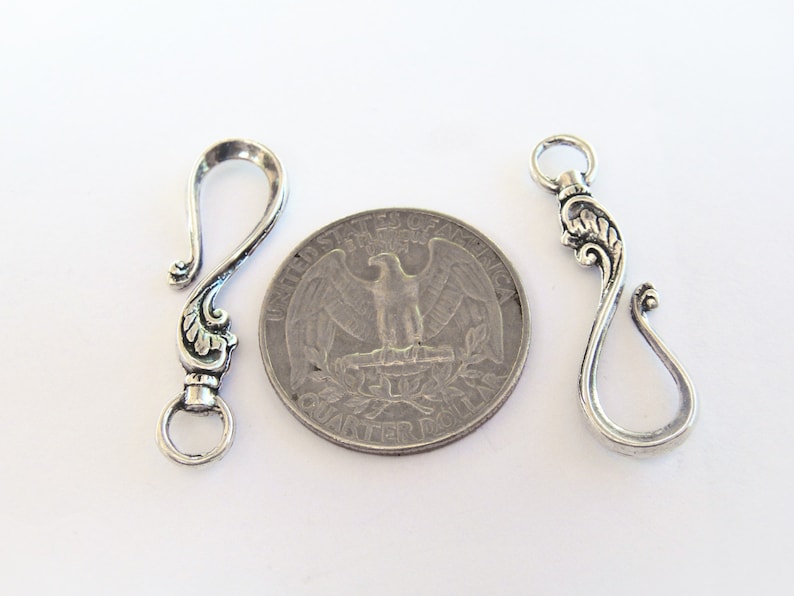 May include: Two silver-toned metal clasps with ornate designs. The clasps are about the size of a US quarter.
