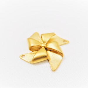 May include: Gold-toned metal charm shaped like a bow with four points. The charm has two holes for attaching to jewelry or other crafts.