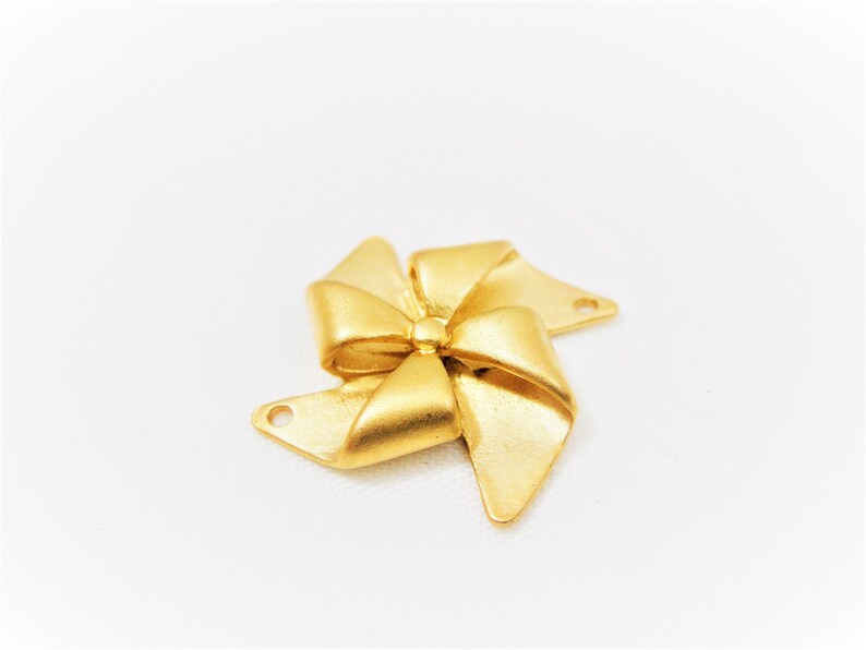 May include: Gold-toned metal charm shaped like a bow with four points. The charm has two holes for attaching to jewelry or other crafts.