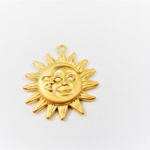 May include: Gold-toned metal charm featuring a sun and moon design. The sun has a face and the moon is crescent shaped. The charm has a loop at the top for attaching to a necklace or bracelet.