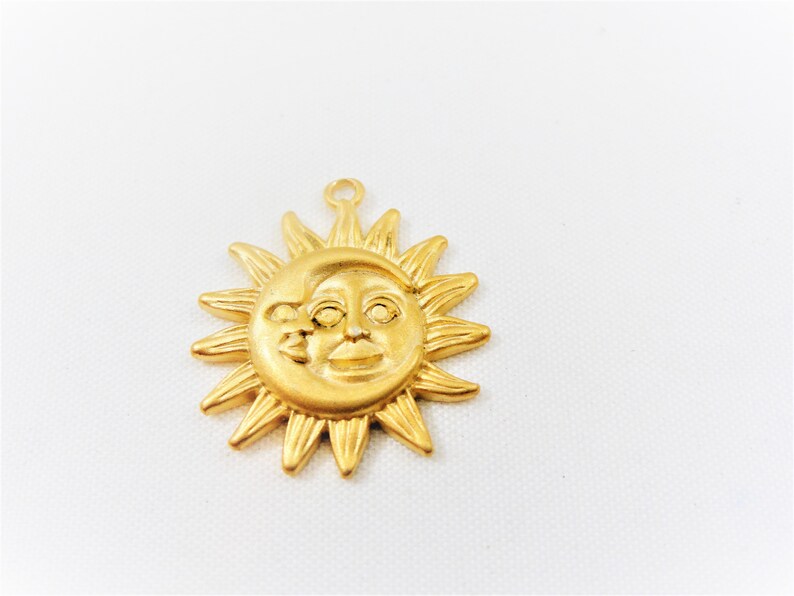 May include: Gold-toned metal charm featuring a sun and moon design. The sun has a face and the moon is crescent shaped. The charm has a loop at the top for attaching to a necklace or bracelet.